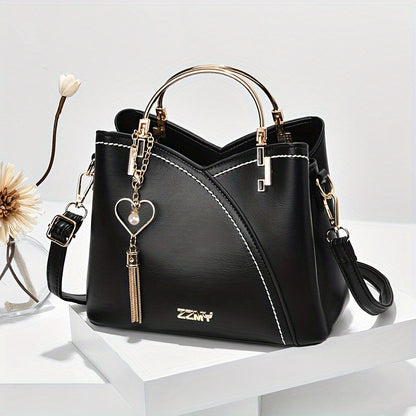 Black handbag with gold accents and a heart-shaped keychain on a white surface.
