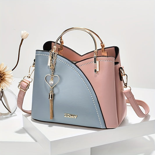 Two-tone pink and blue handbag with a heart keychain on a white surface.