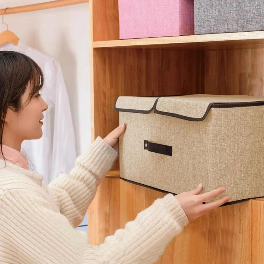 Person holding a beige storage box in front of a wooden shelf with clothes.