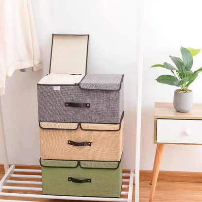 Stack of three fabric storage boxes in gray, beige, and green with handles in a room setting.