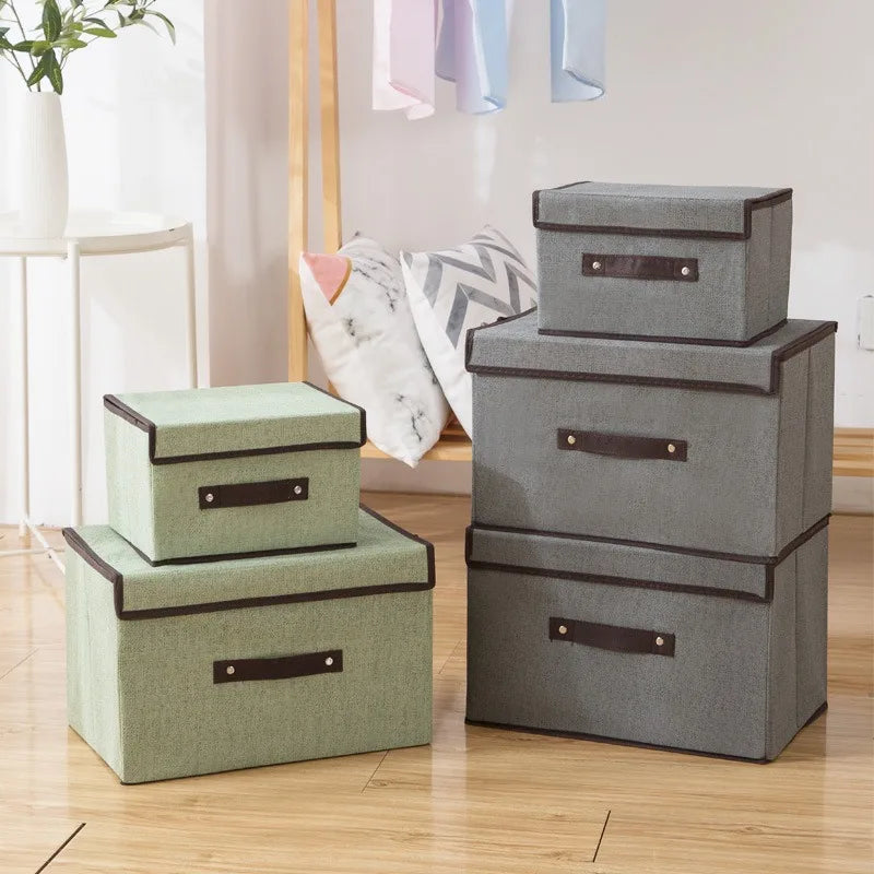 Set of gray and green storage boxes with brown handles on a wooden floor.