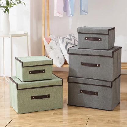 Set of gray and green storage boxes with brown handles on a wooden floor.