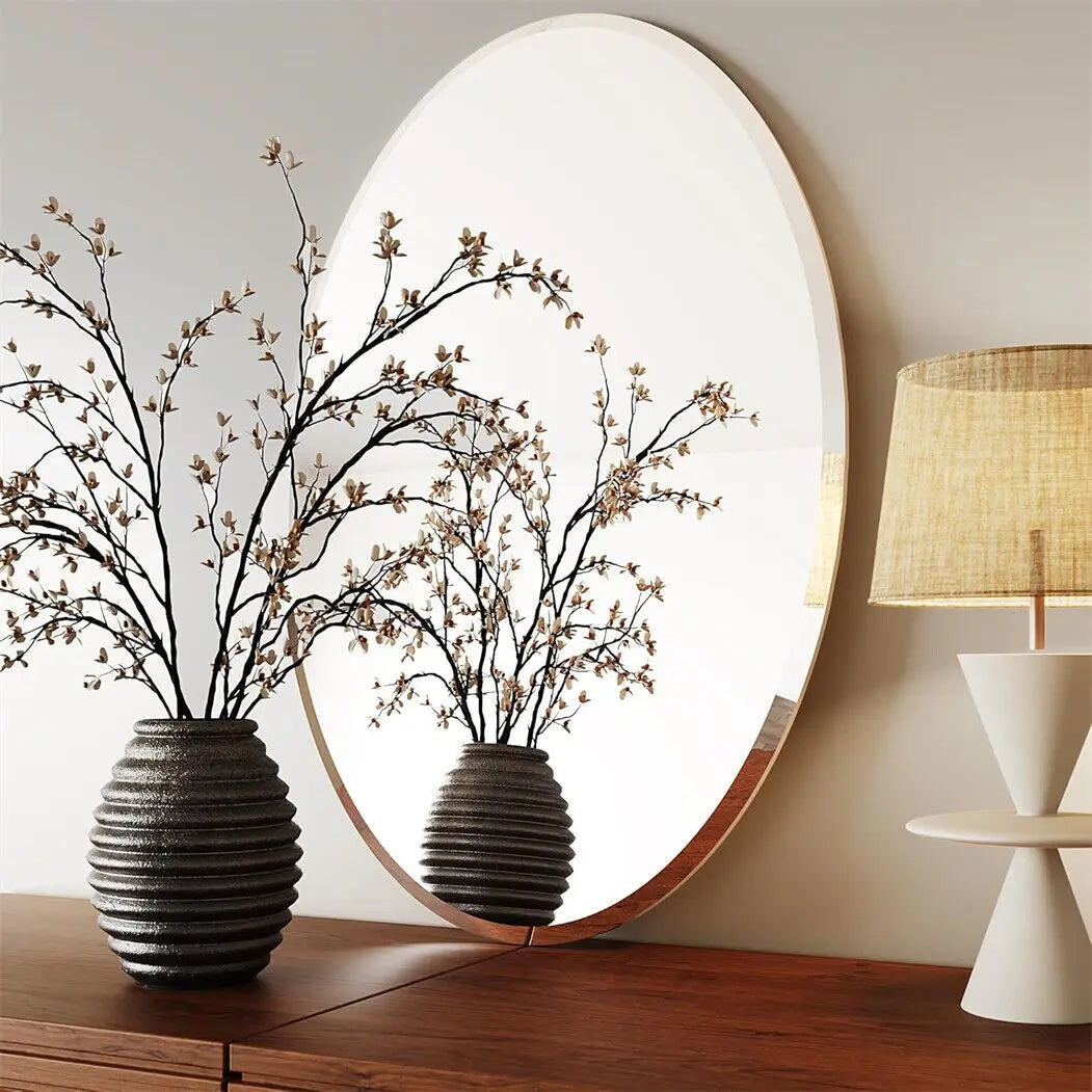 Two dark vases with branches on a wooden surface, large round mirror, and white lamp in the background.
