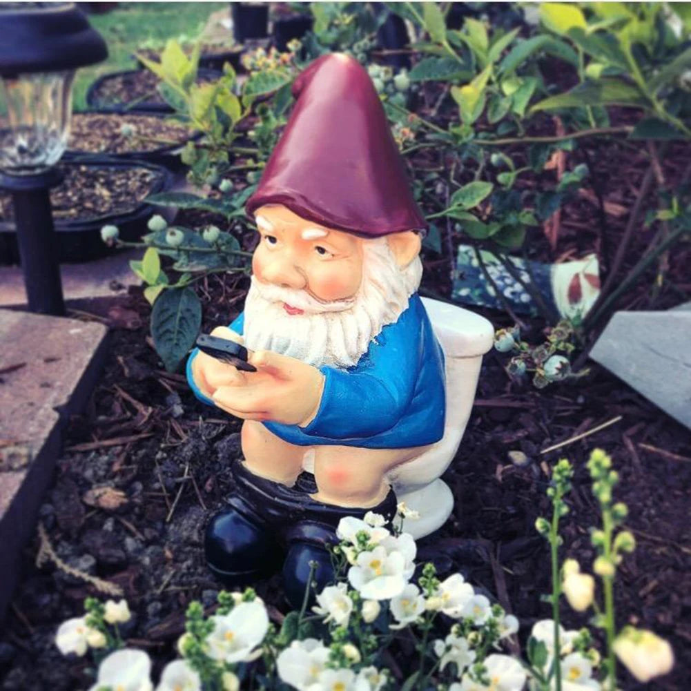 Gnome figurine on a toilet in a garden setting with flowers and plants.