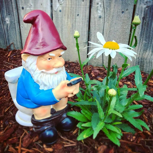 Gnome figurine using a smartphone next to a flower plant