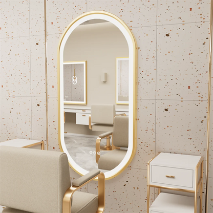 Oval-shaped mirror with gold frame in a room with beige chairs and furniture.