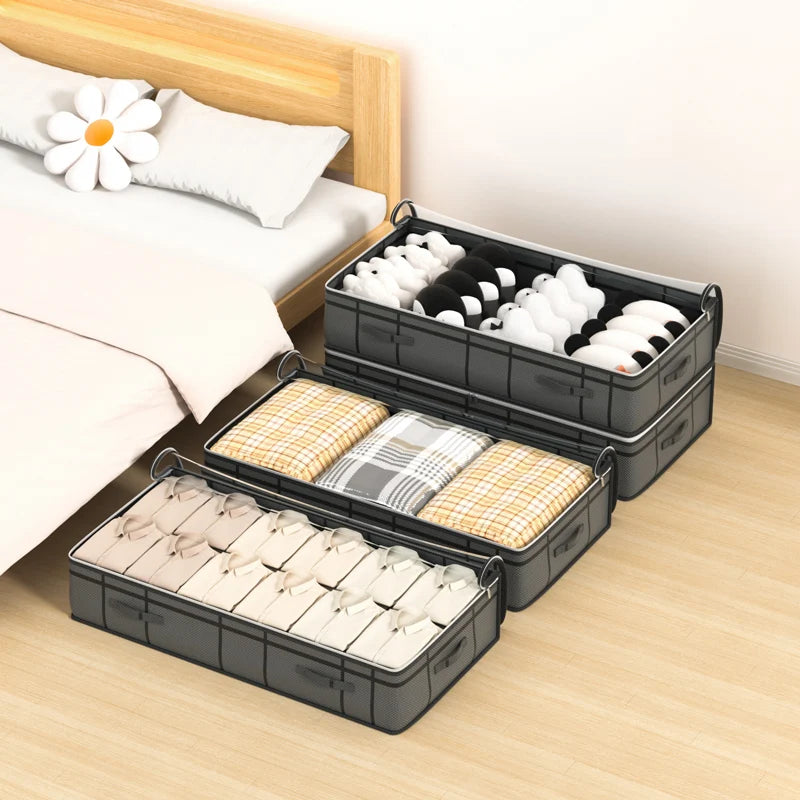 Stack of black storage boxes under a bed with neatly folded clothes inside.
