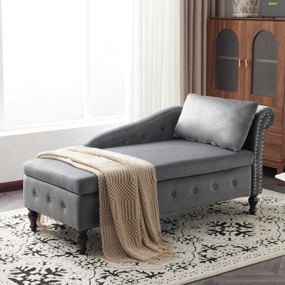 Gray tufted chaise lounge with a beige blanket on a patterned rug in a room with a wooden cabinet.