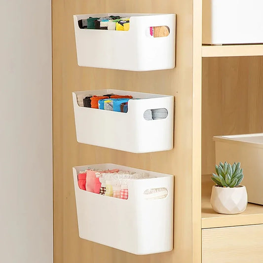White storage bins hanging on a wooden shelf with books and a plant.