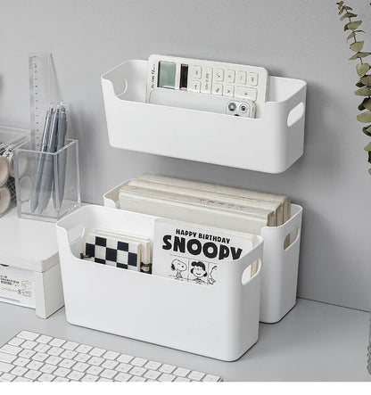 White storage baskets on a desk with books and stationery items.