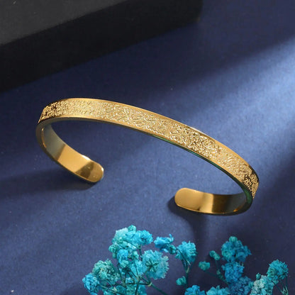Gold bracelet with intricate design on a dark blue background with turquoise flowers.