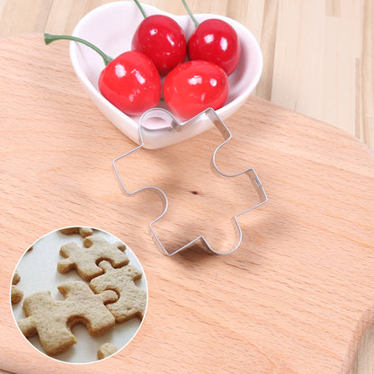 Metal puzzle piece cookie cutter on a wooden surface with a bowl of cherries in the background.