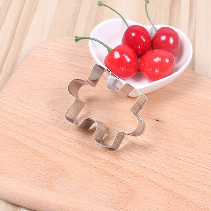 Metal puzzle piece cookie cutter on a wooden surface with red cherries in the background.