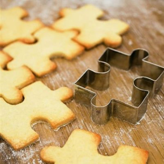 Jigsaw puzzle-shaped cookies with a metal cookie cutter on a wooden surface