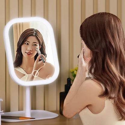Woman applying makeup in front of a lighted vanity mirror.