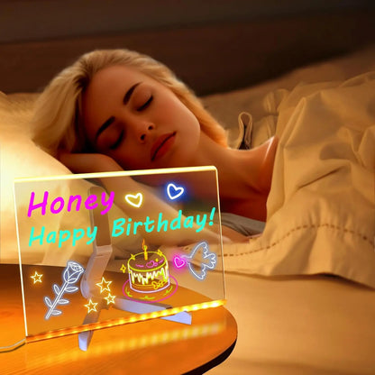 Woman lying in bed with a glowing sign that says 'Honey Happy Birthday!' on a wooden nightstand.