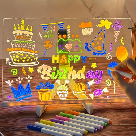 Transparent board with colorful birthday-themed drawings and 'Happy Birthday' text, illuminated by LED lights, on a wooden surface.