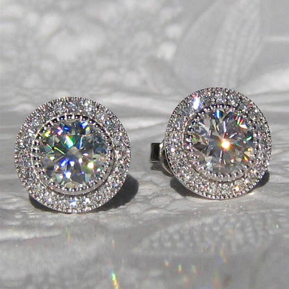 Pair of silver stud earrings with clear gemstones on a reflective surface.