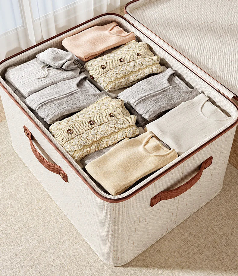 Beige storage bin with brown handles filled with folded clothes on a light surface.
