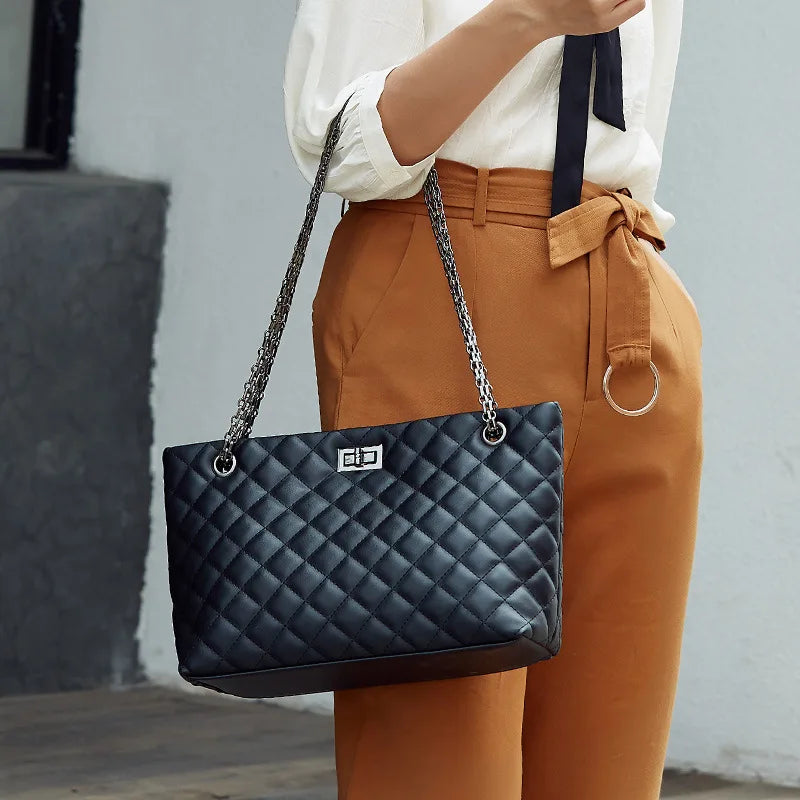 Person holding a black quilted handbag with a chain strap against a neutral background