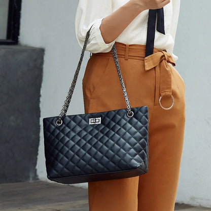 Person holding a black quilted handbag with a chain strap against a neutral background