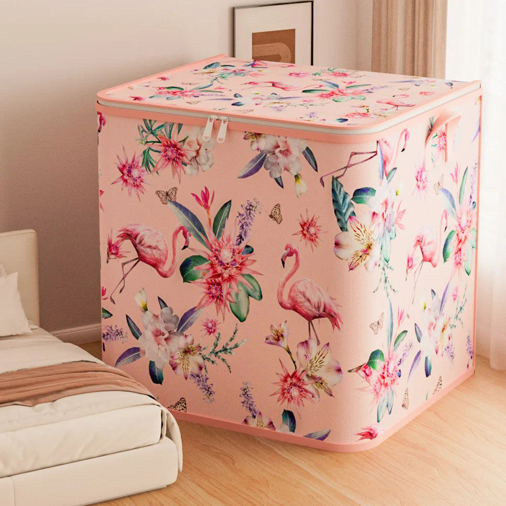Floral-patterned laundry basket with flamingos on a wooden floor next to a bed.