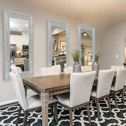 Dining room with wooden table and white chairs, featuring three large decorative mirrors on the wall.