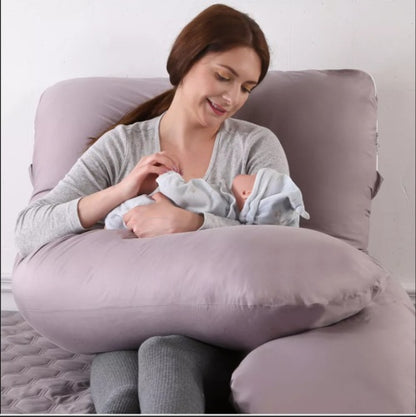Woman holding a baby while sitting on a large U-shaped pillow against a white background