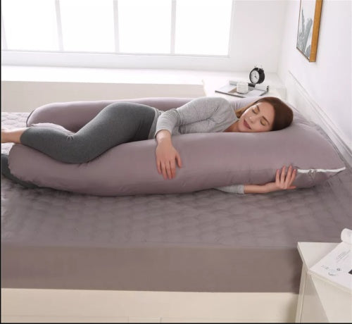 Woman lying on a large U-shaped body pillow in a bedroom.