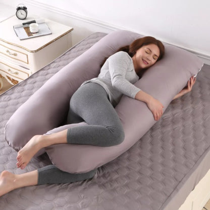 Woman lying on a U-shaped body pillow in a bedroom setting.