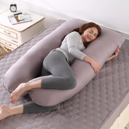 Woman lying on a U-shaped body pillow in a bedroom setting.