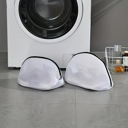 Two white mesh laundry bags with black zippers on a gray floor in front of a washing machine.