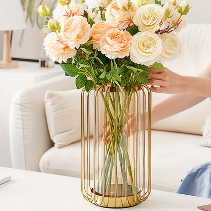 Person holding a bouquet of flowers in a gold vase on a table with a white couch in the background