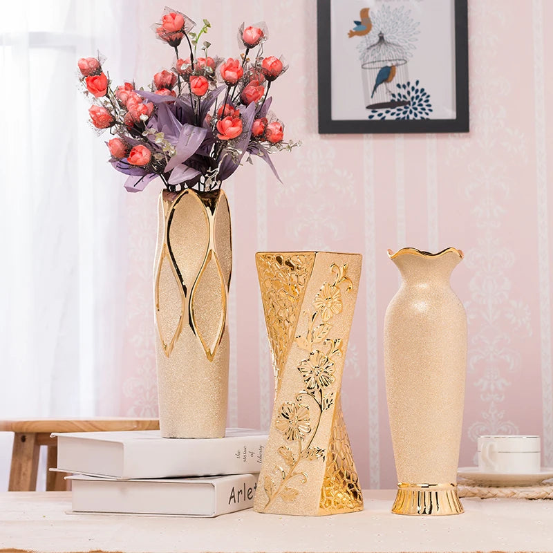 Three decorative vases on a surface with a vase containing flowers in the background.