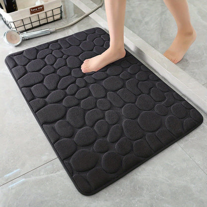 Black textured bath mat on a bathroom floor with a foot stepping onto it.