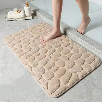 Beige textured bath mat on a bathroom floor with a person stepping onto it.