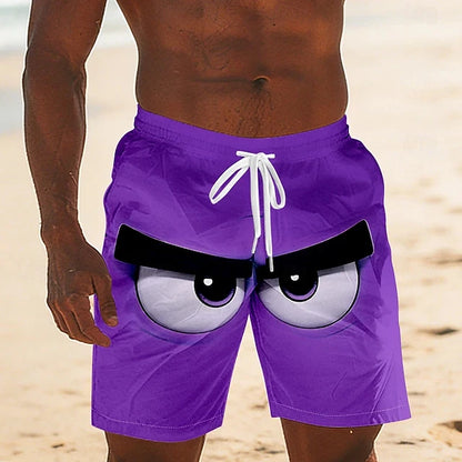 A close-up of a person wearing purple swim trunks with a cartoon angry-eye graphic on the front, standing on a sandy beach.
