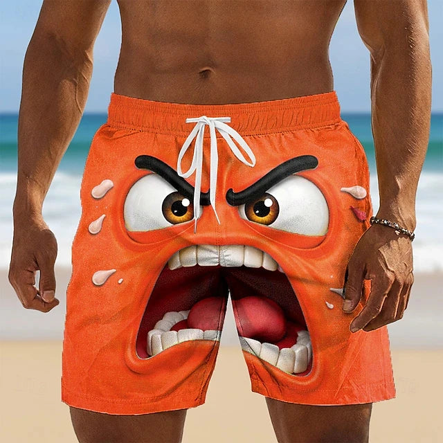 Bright orange swim trunks with a 3D cartoon angry face graphic, worn by a model on a beach background.