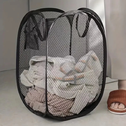 Black mesh laundry basket with clothes inside on a light-colored floor.