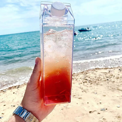 Hand holding a clear container with a red liquid on a beach