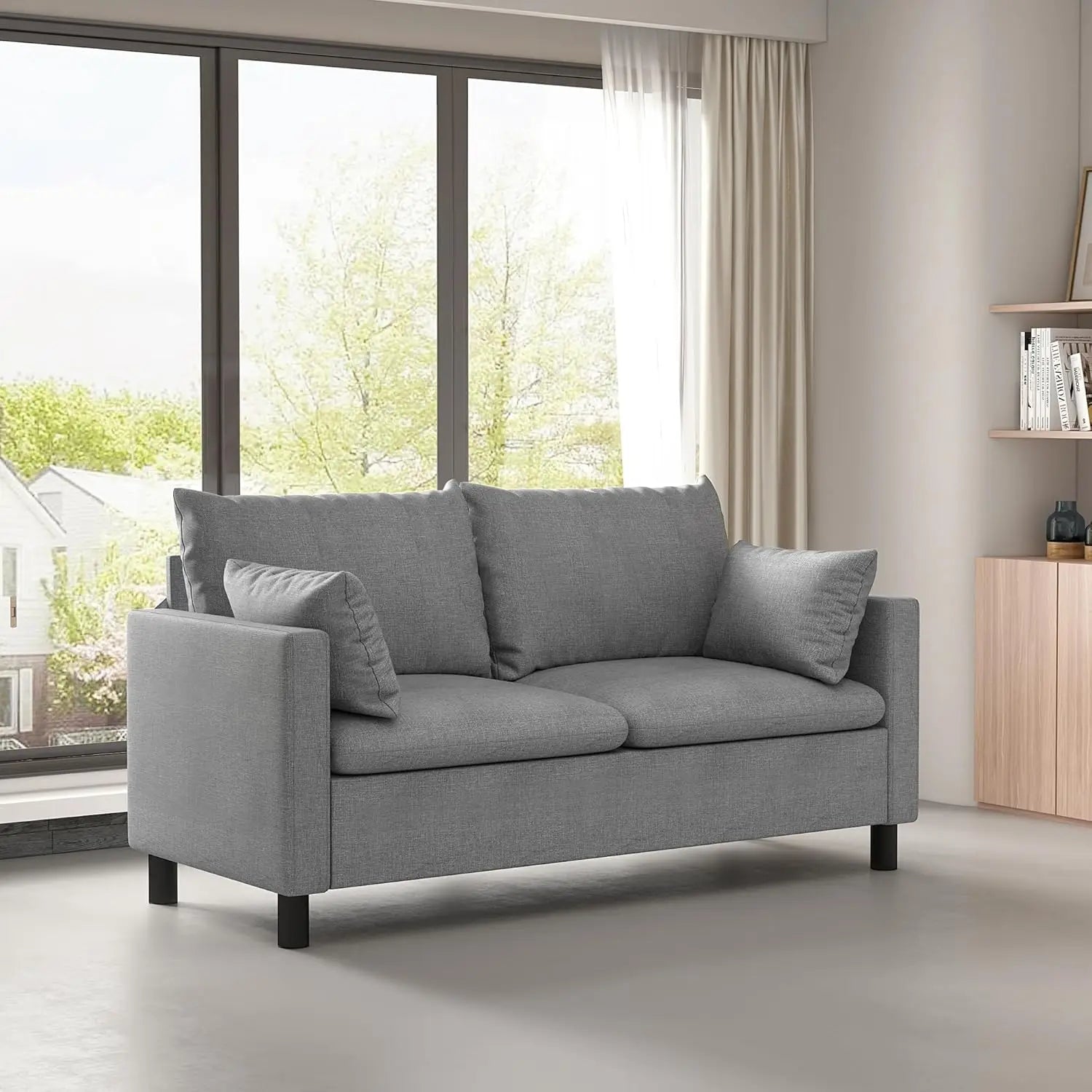 Gray sofa in a modern living room with large windows and a wooden cabinet.