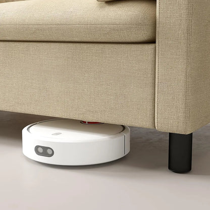Robotic vacuum cleaner under a beige sofa on a light-colored floor