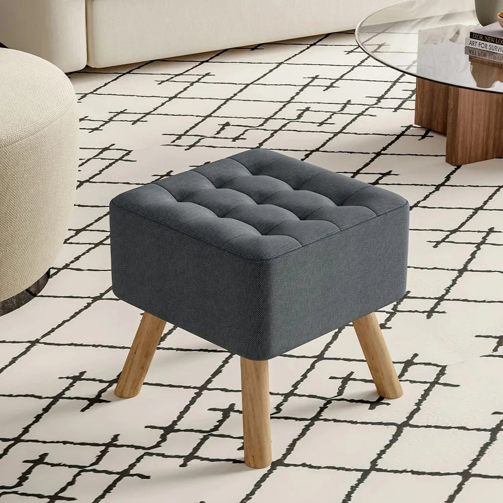 Gray upholstered ottoman with wooden legs on a patterned rug
