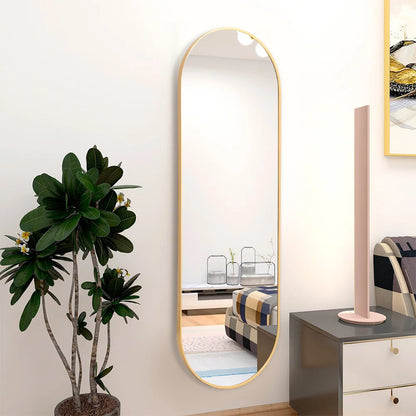 Long mirror with gold frame leaning against a wall next to a plant and dresser.