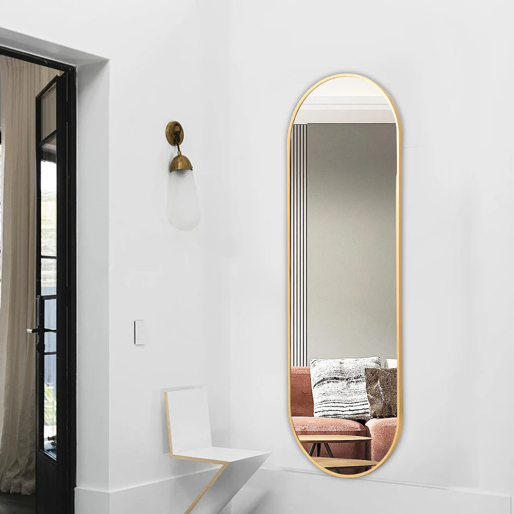 Long, oval-shaped mirror with gold frame on a white wall in a modern interior setting.