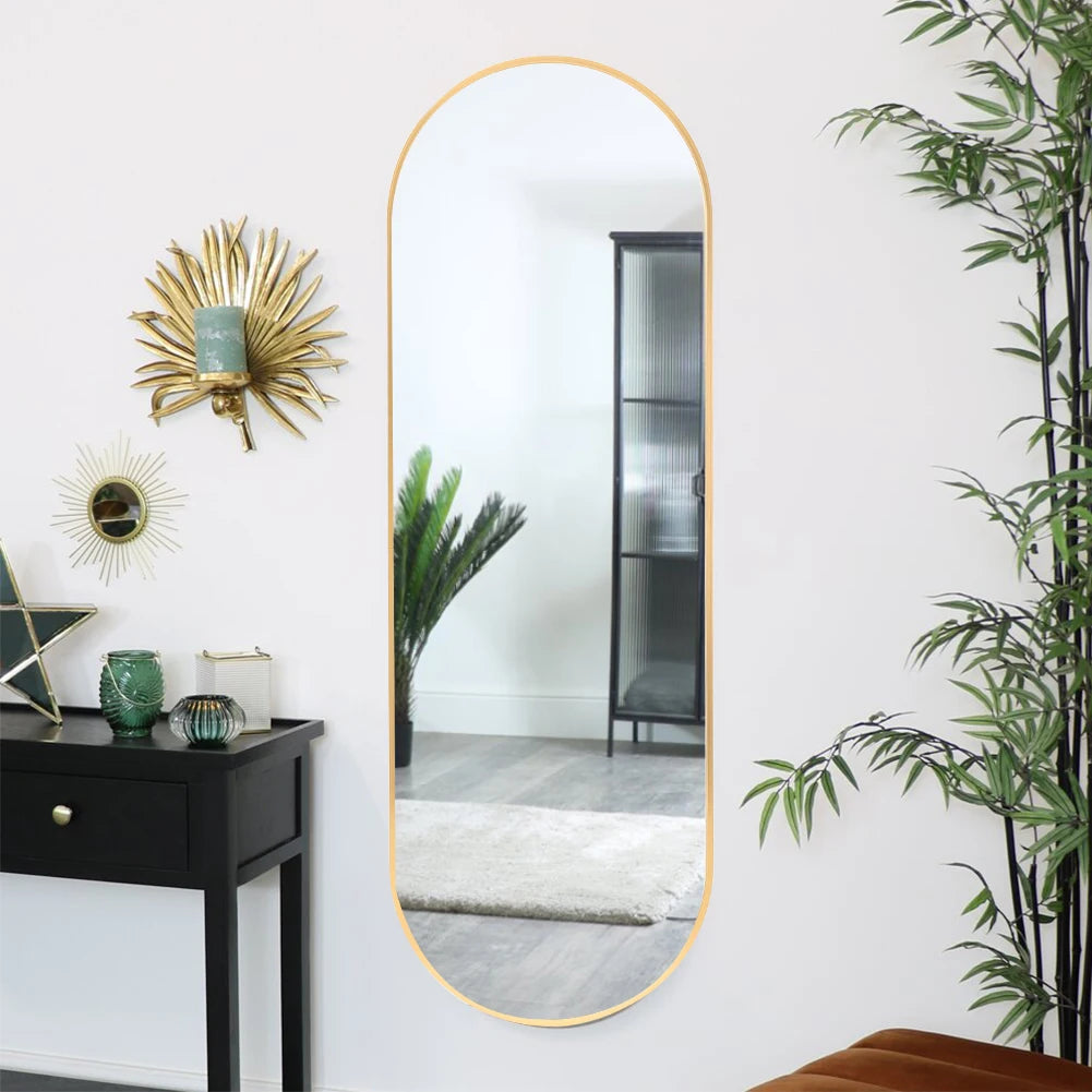 Long vertical mirror with gold frame on a white wall with decorative elements.