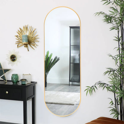Long vertical mirror with gold frame on a white wall with decorative elements.