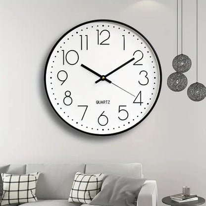 Round wall clock on a white wall above a gray sofa with patterned cushions.