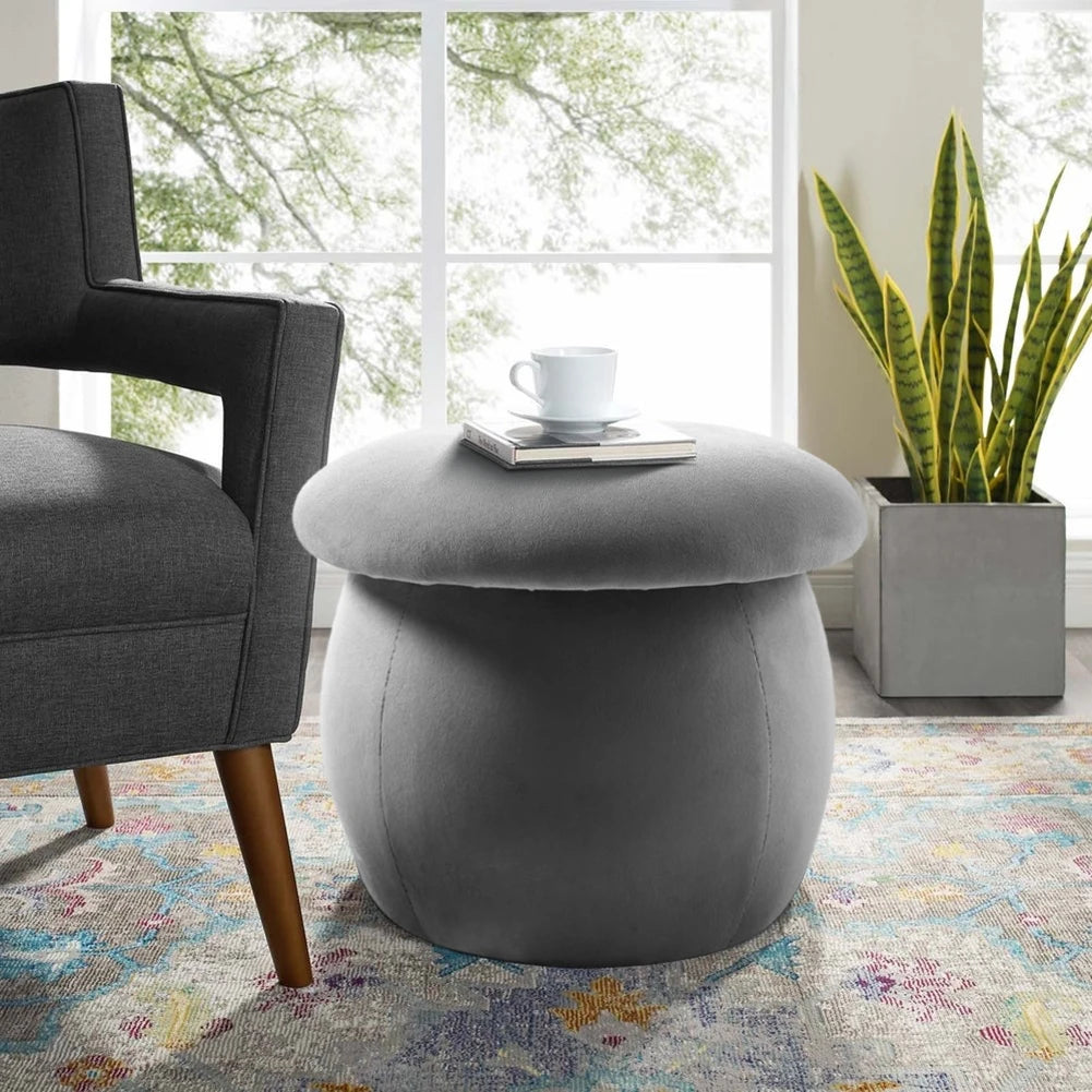 Gray ottoman with a cup and book on top, next to a gray chair and plant in a living room.