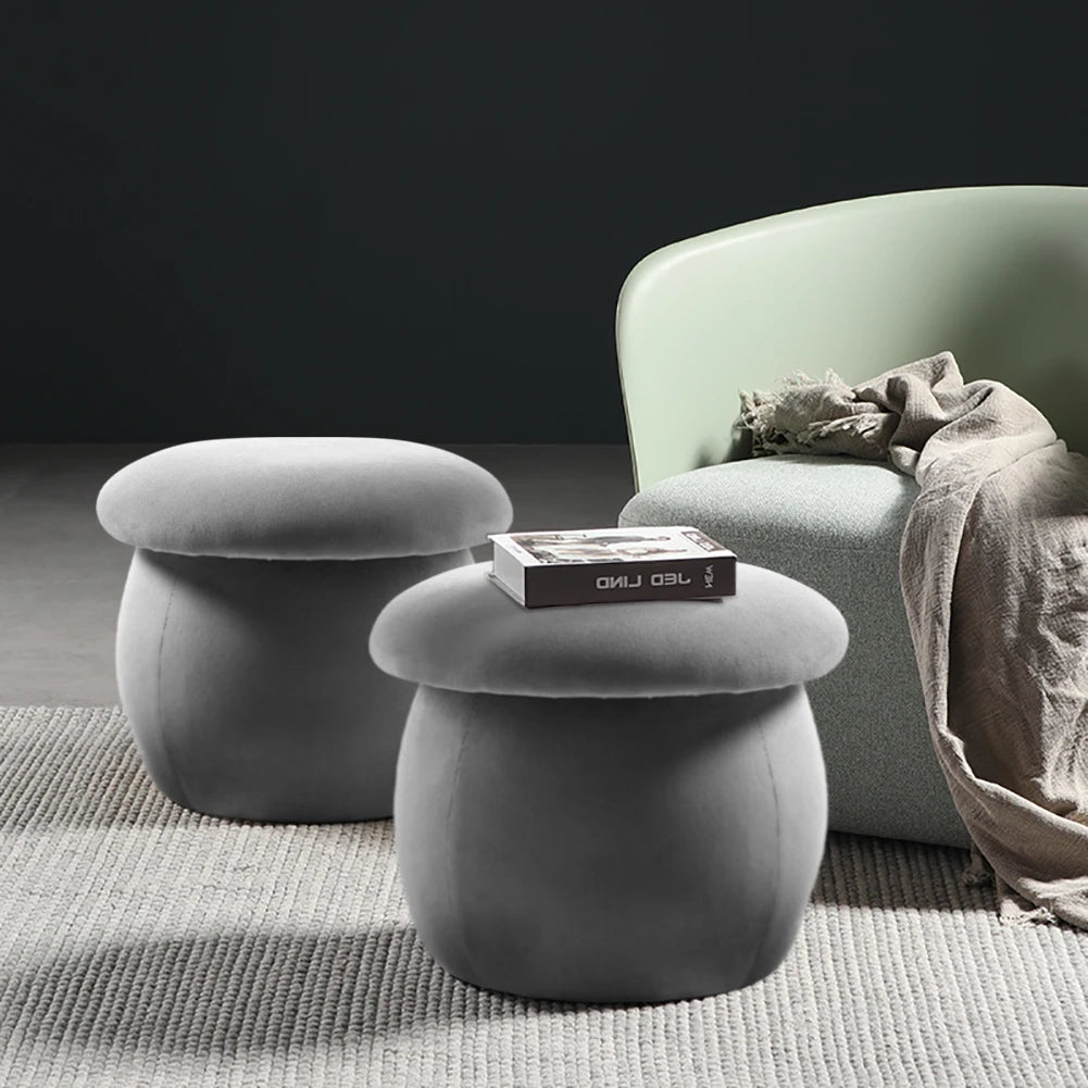 Two gray mushroom-shaped stools in front of a green armchair with a blanket on a dark background
